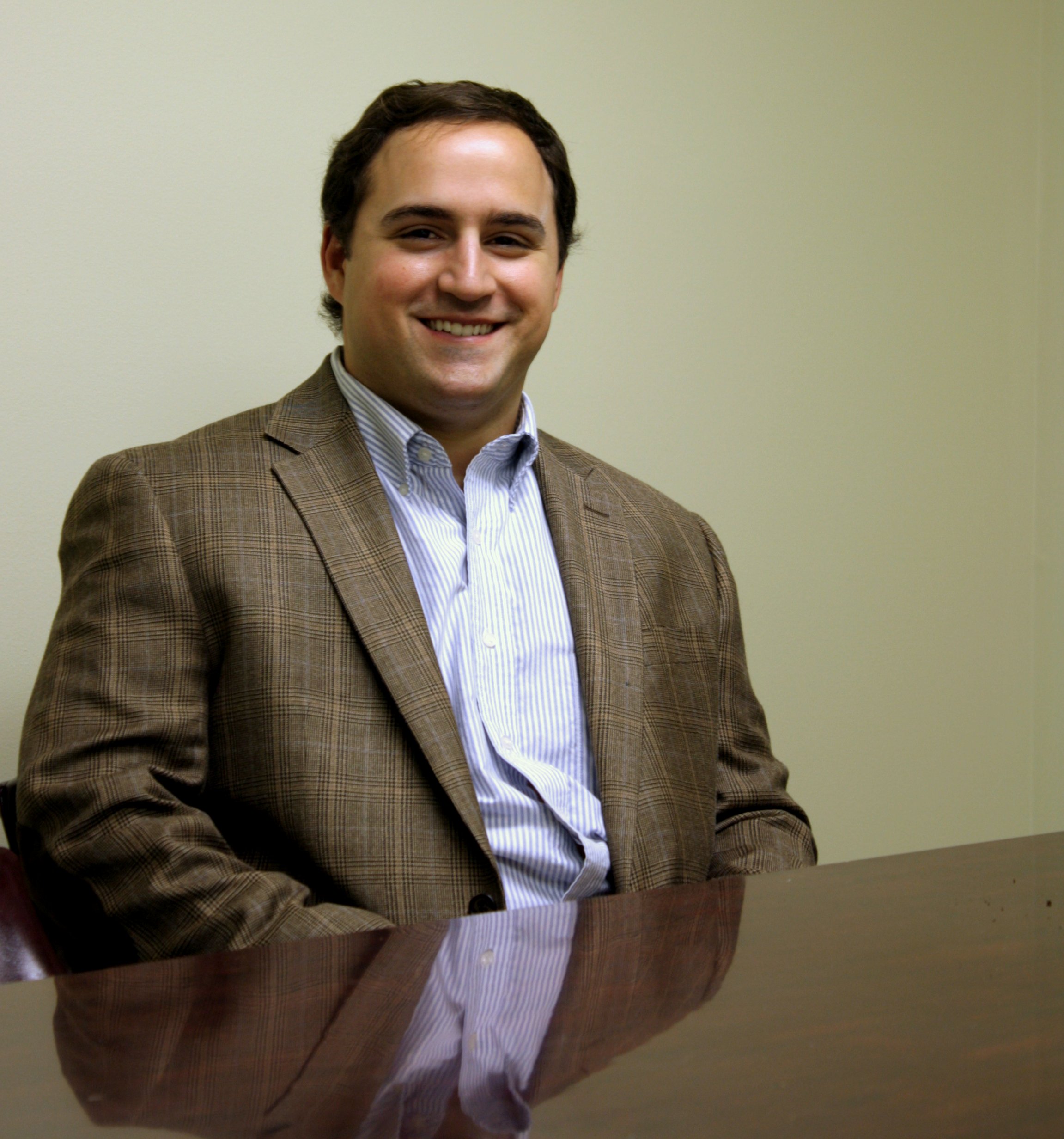 Adam Maniscalco, an attorney at law with and founding partner of Baxley Maniscalco, sits at a desk and poses for a photo.