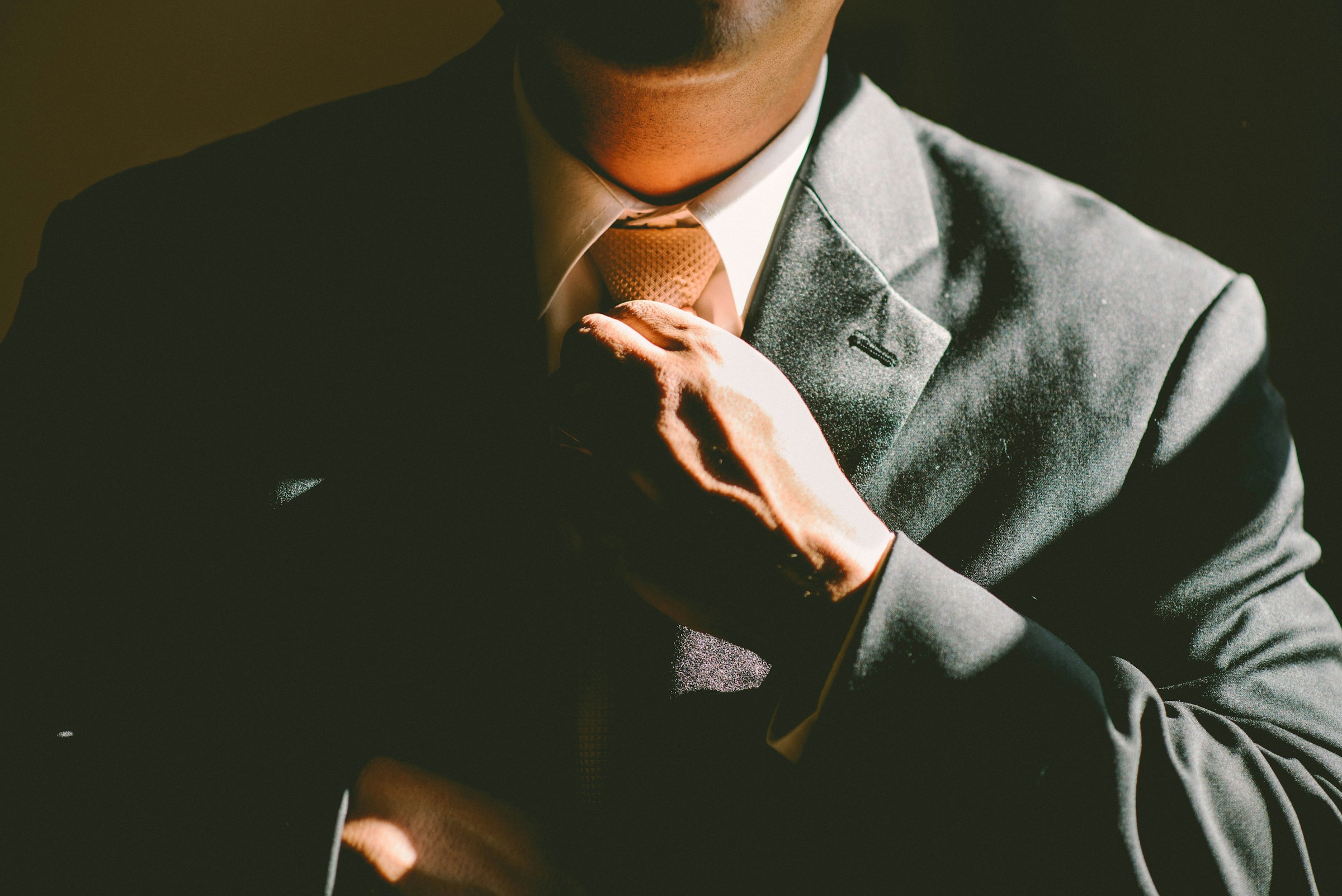 A man in a tuxedo is seen adjusting his tie in a dark room.