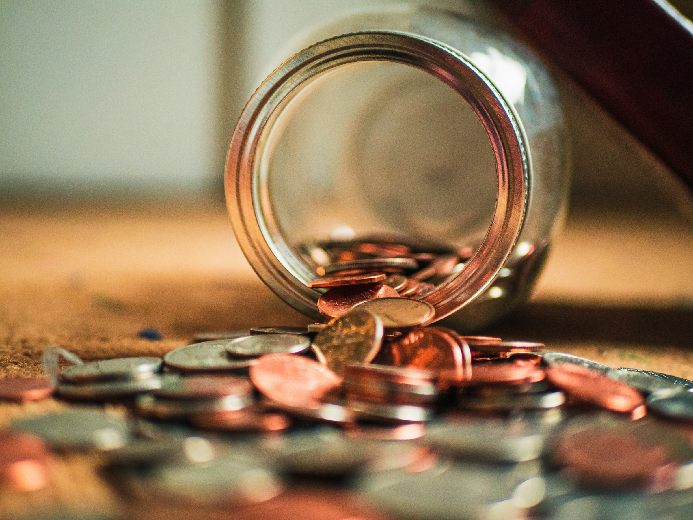 A jar of change is seen spilled out over a table.