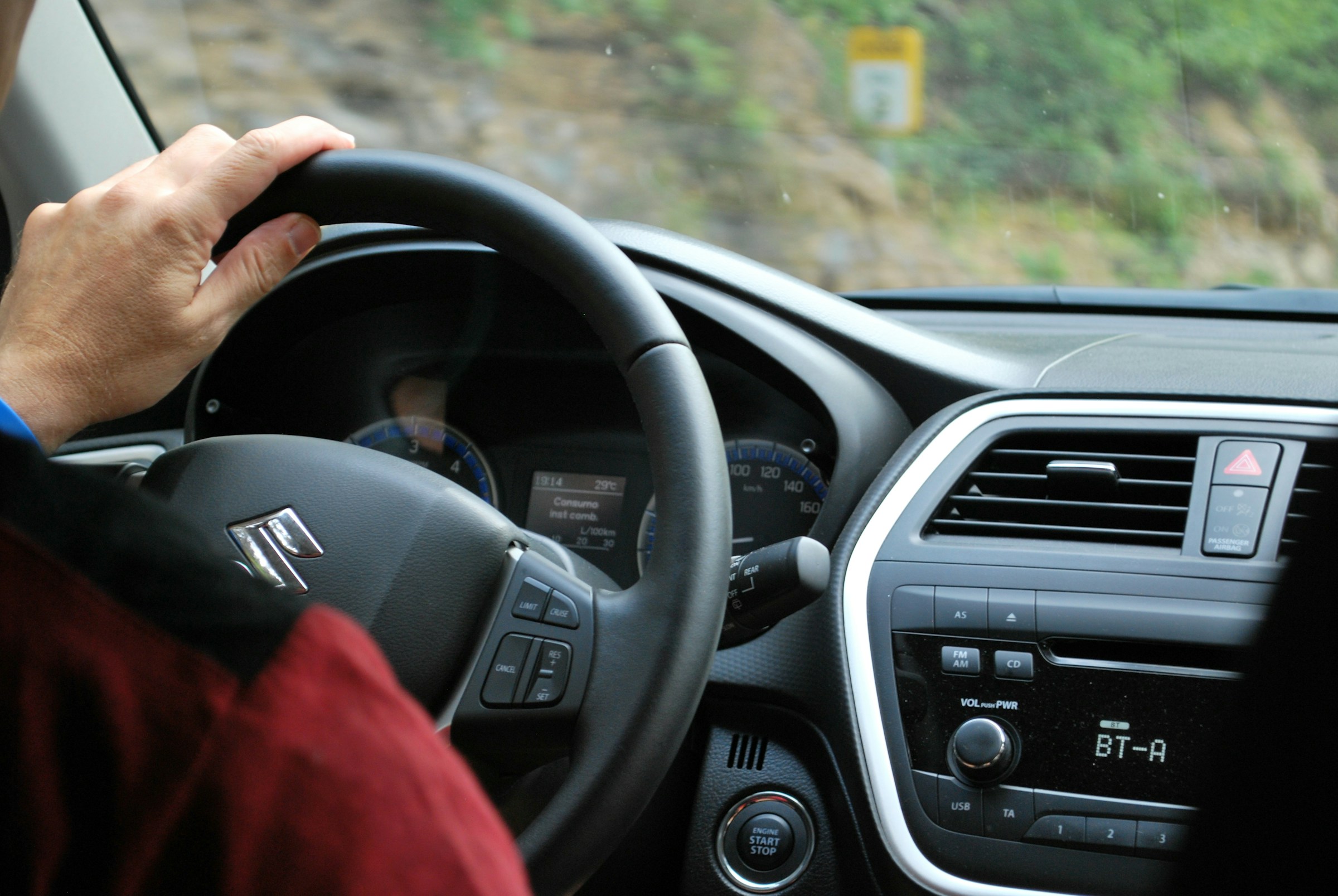 A closeup image of a driver's hand on the steering wheel of their car.