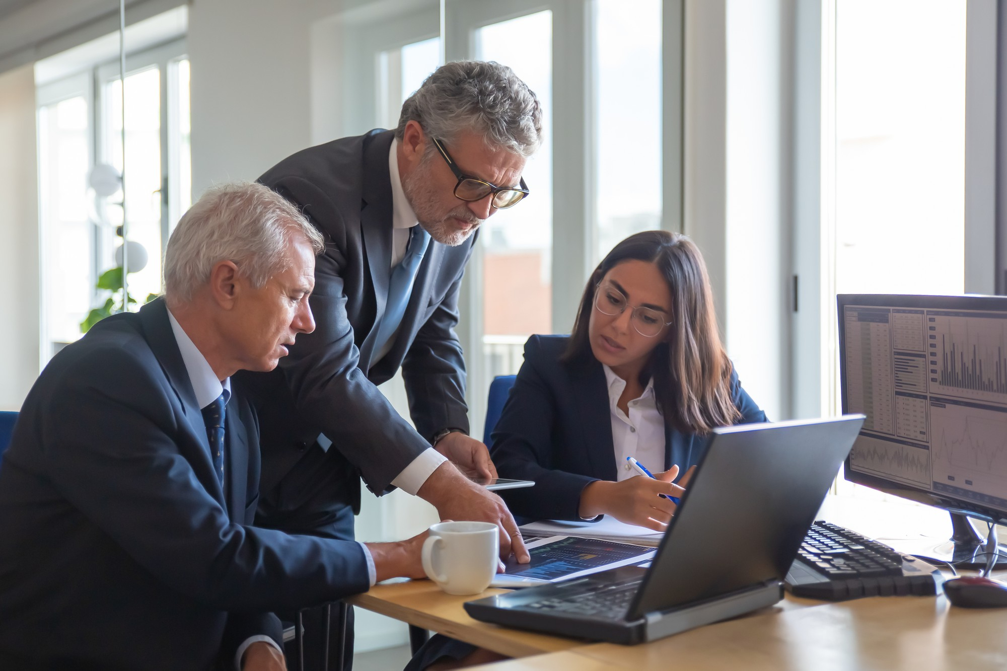 A personal injury lawyer stands over two people sitting at a desk, helping them with their case.