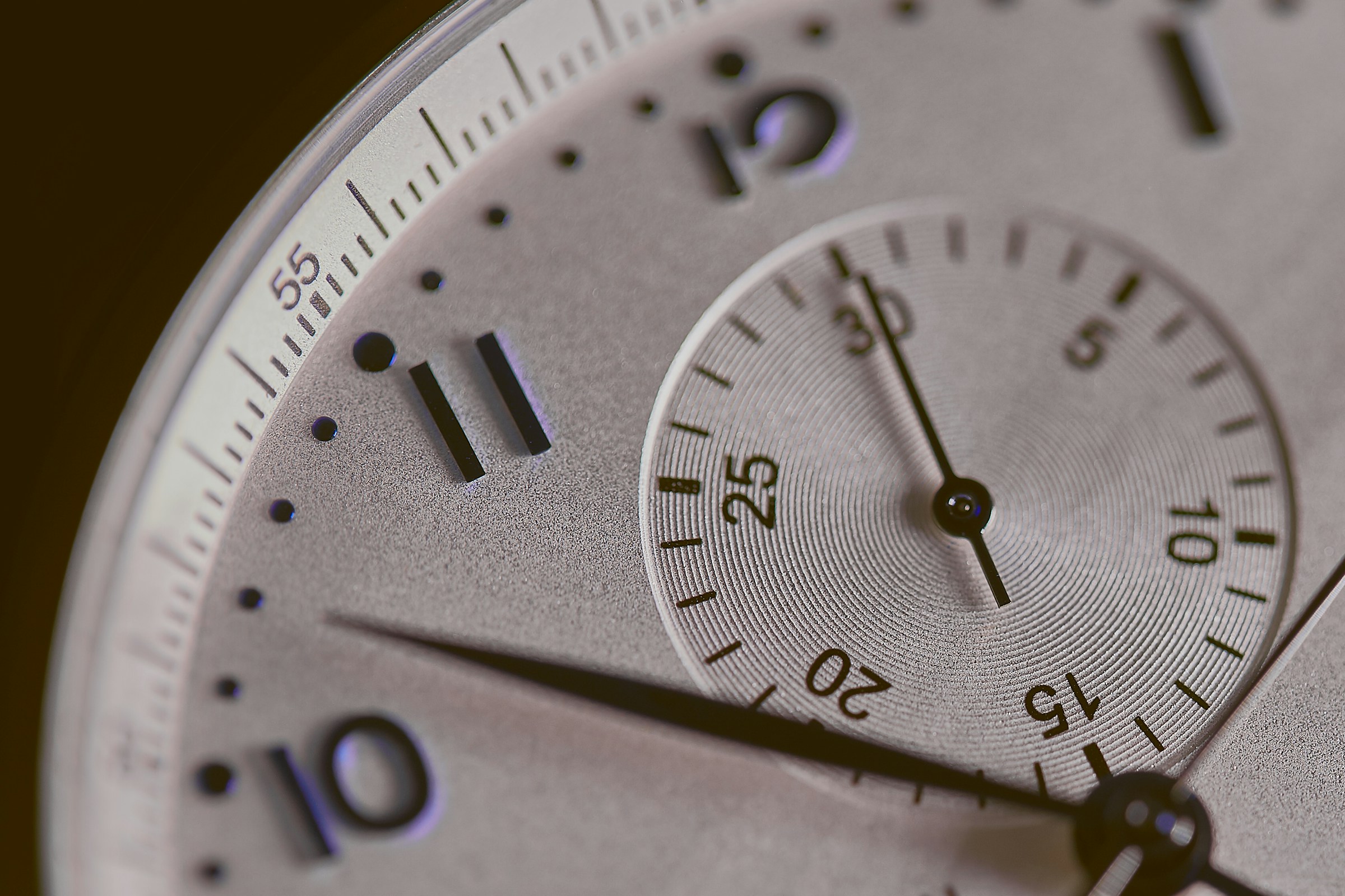 A close up of a dial on a wristwatch. We also see a chronograph on the dial, and the dial is white with blue numbers.